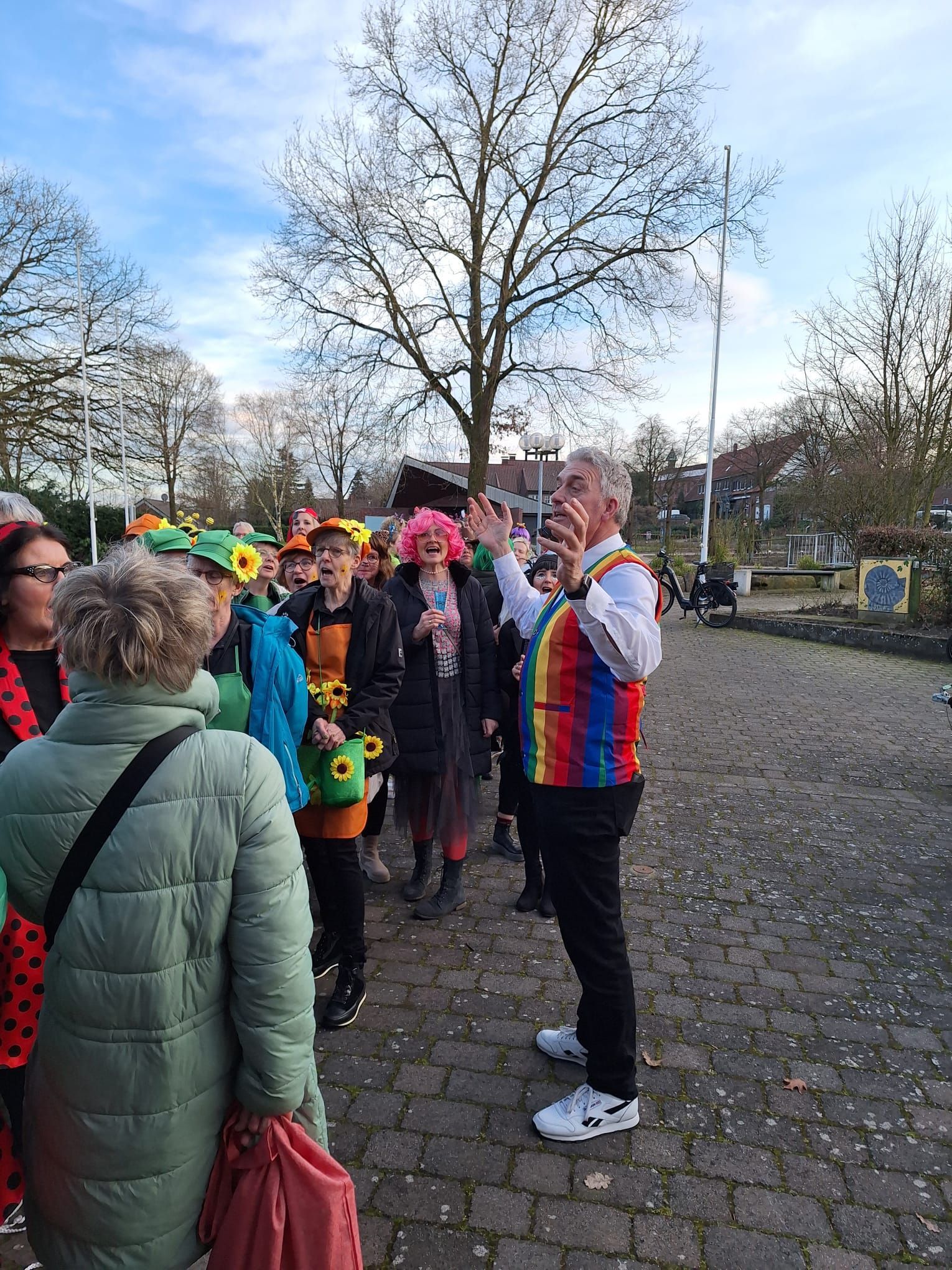 Ein Mann in einer bunten Weste steht vor einer Gruppe von Menschen.