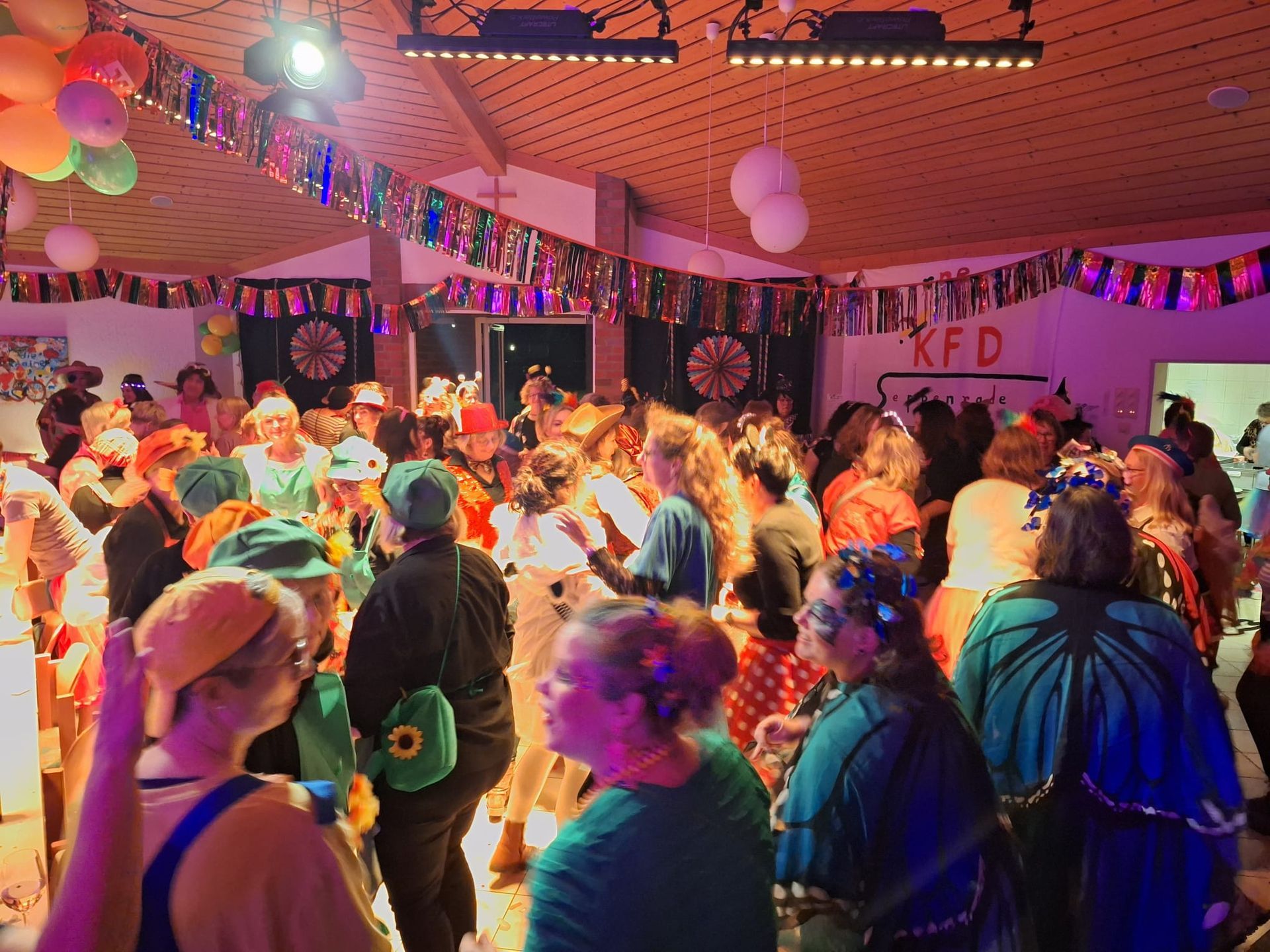 Eine große Gruppe von Menschen tanzt in einem mit Luftballons und Bannern dekorierten Raum.