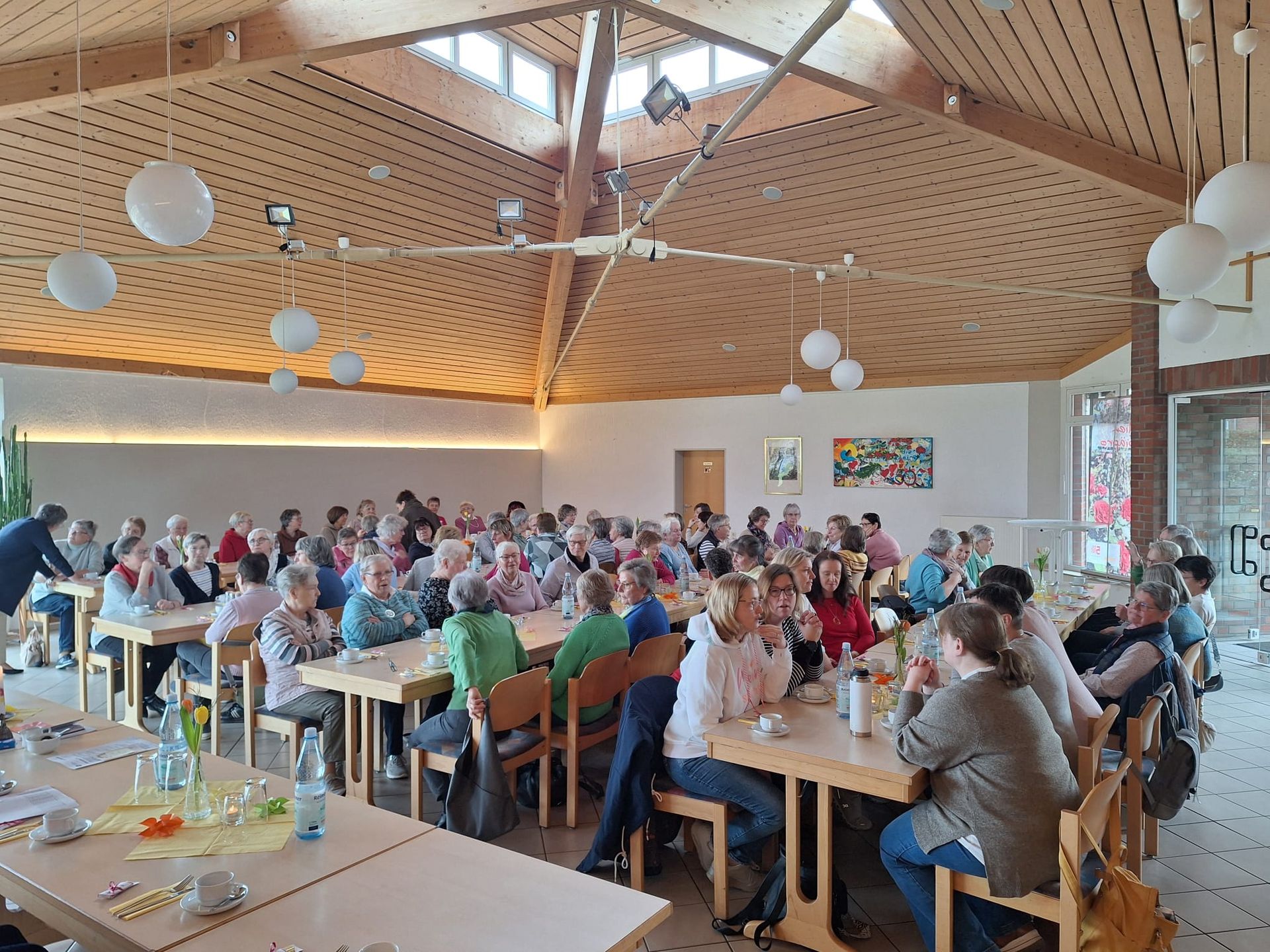 Eine große Gruppe von Menschen sitzt in einem großen Raum an Tischen.