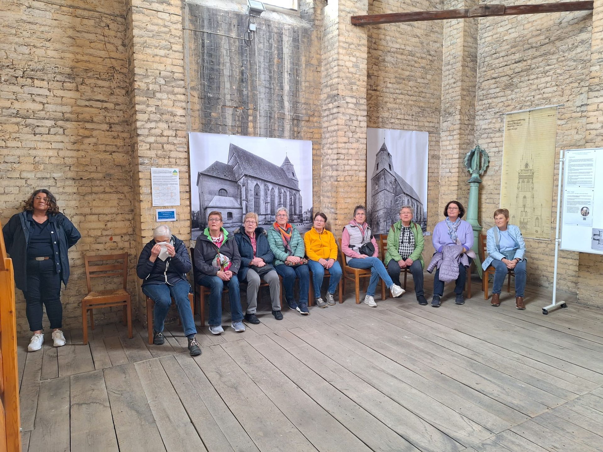 Eine Gruppe von Menschen sitzt in einem Raum vor einer Backsteinmauer.