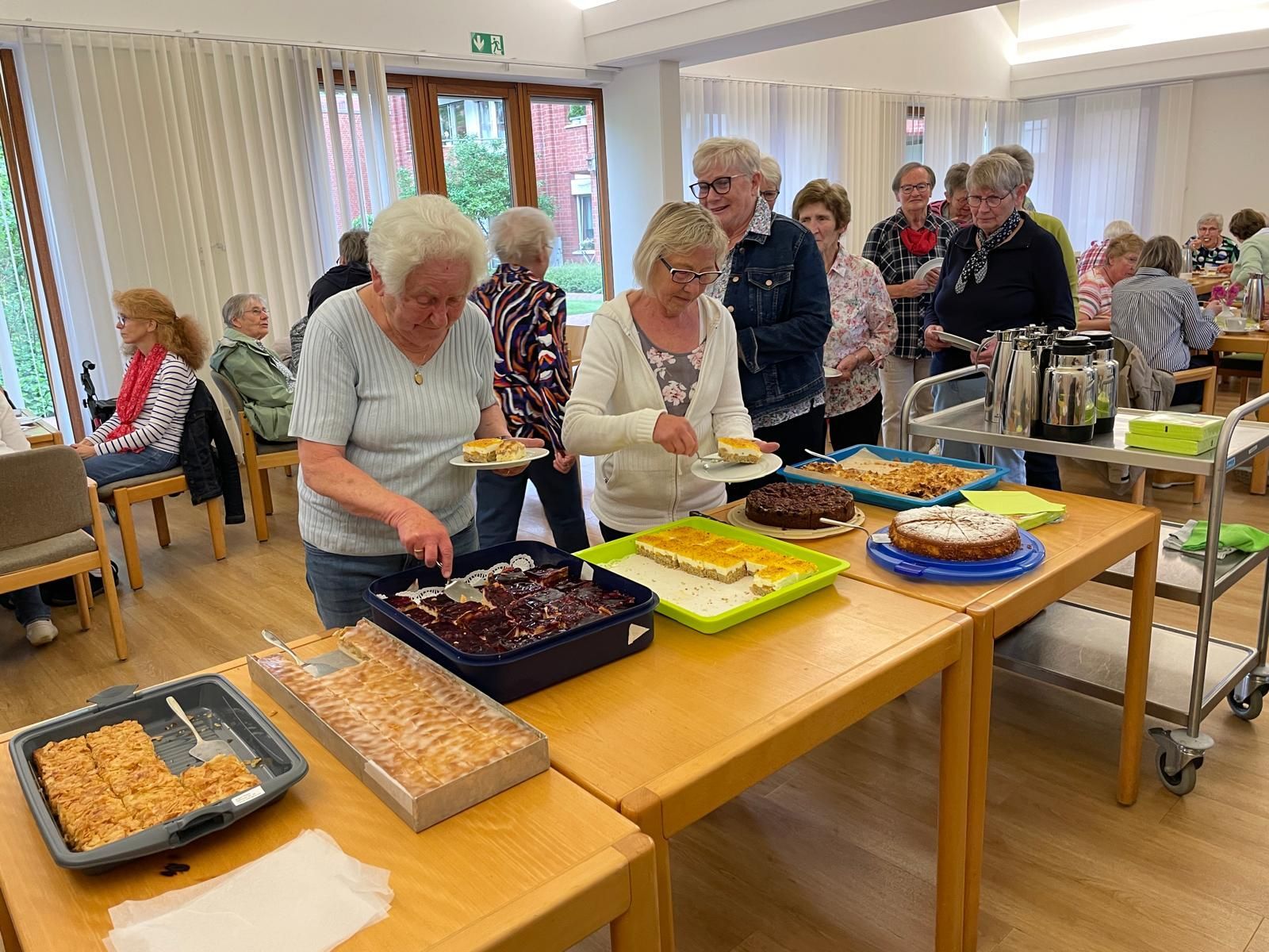 Eine Gruppe von Menschen steht mit Tellern voller Essen um einen Tisch herum.