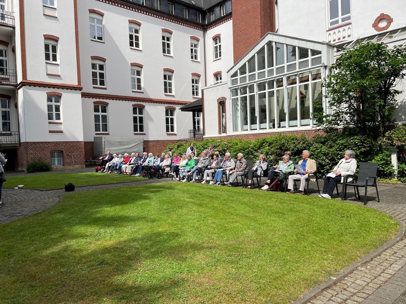 Eine Gruppe von Menschen sitzt auf dem Rasen vor einem Gebäude.