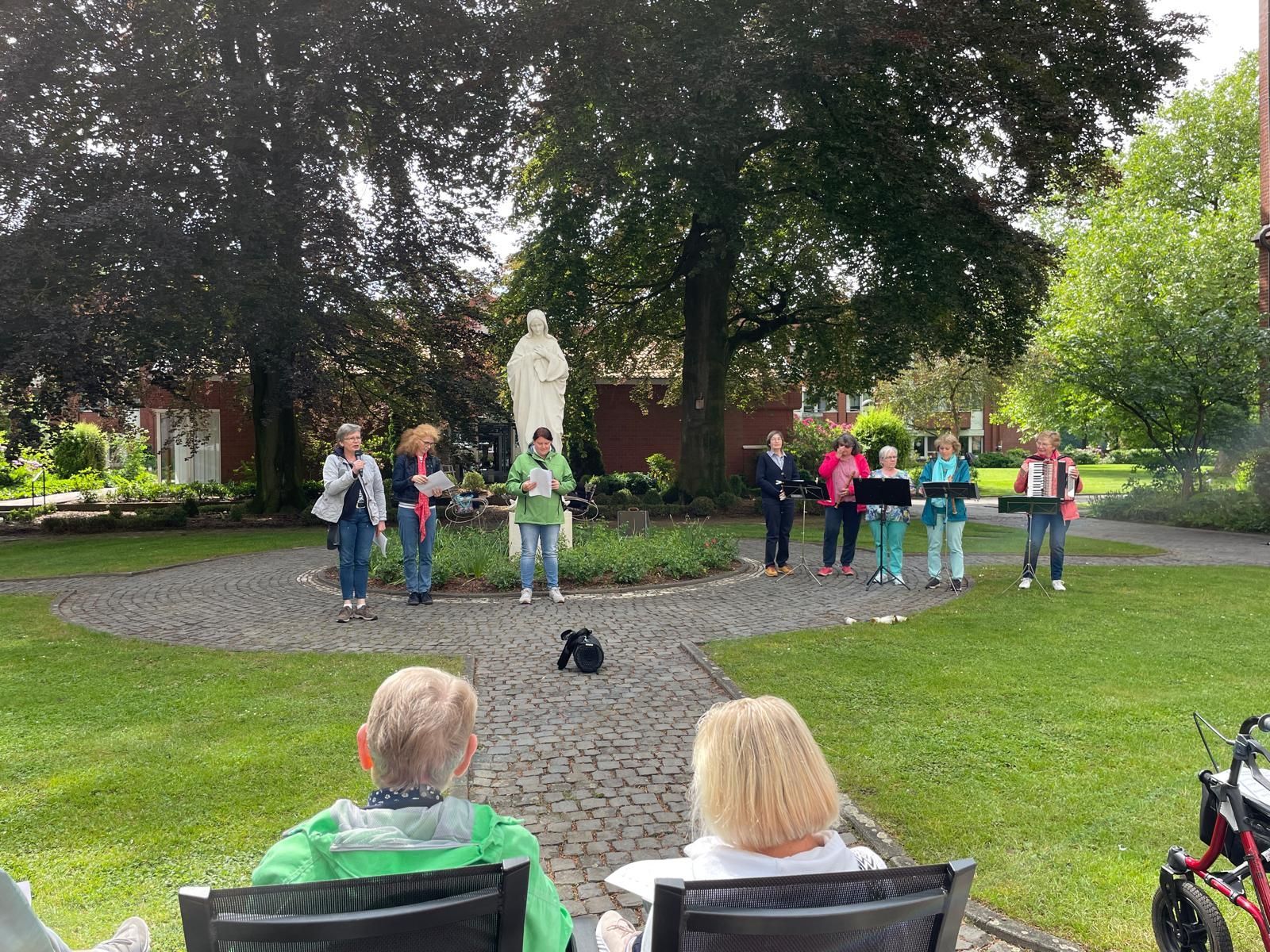 Eine Gruppe von Menschen sitzt auf Bänken vor einer Statue in einem Park.