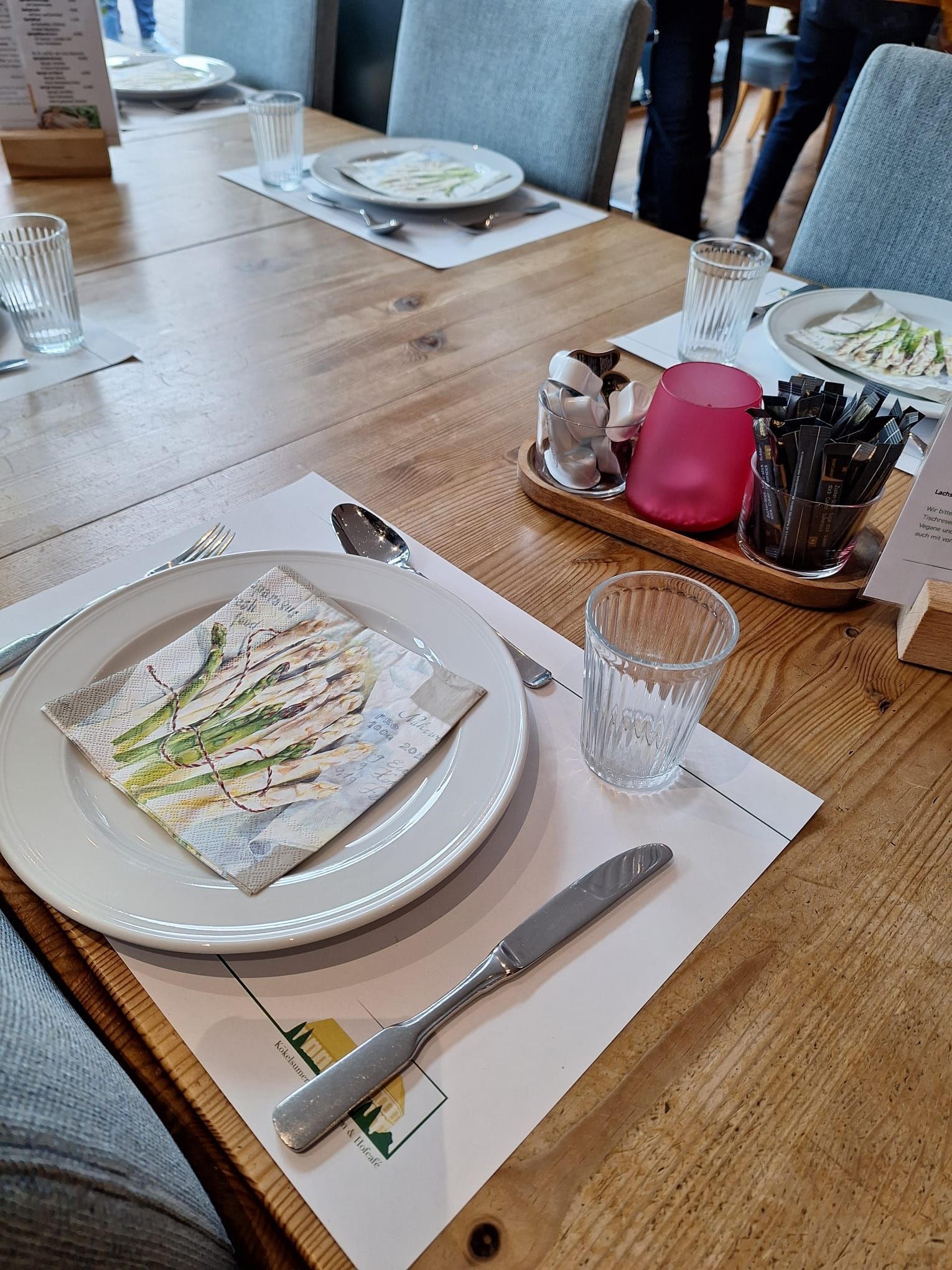 Ein Holztisch mit Tellern, Servietten, Gläsern und Besteck darauf.