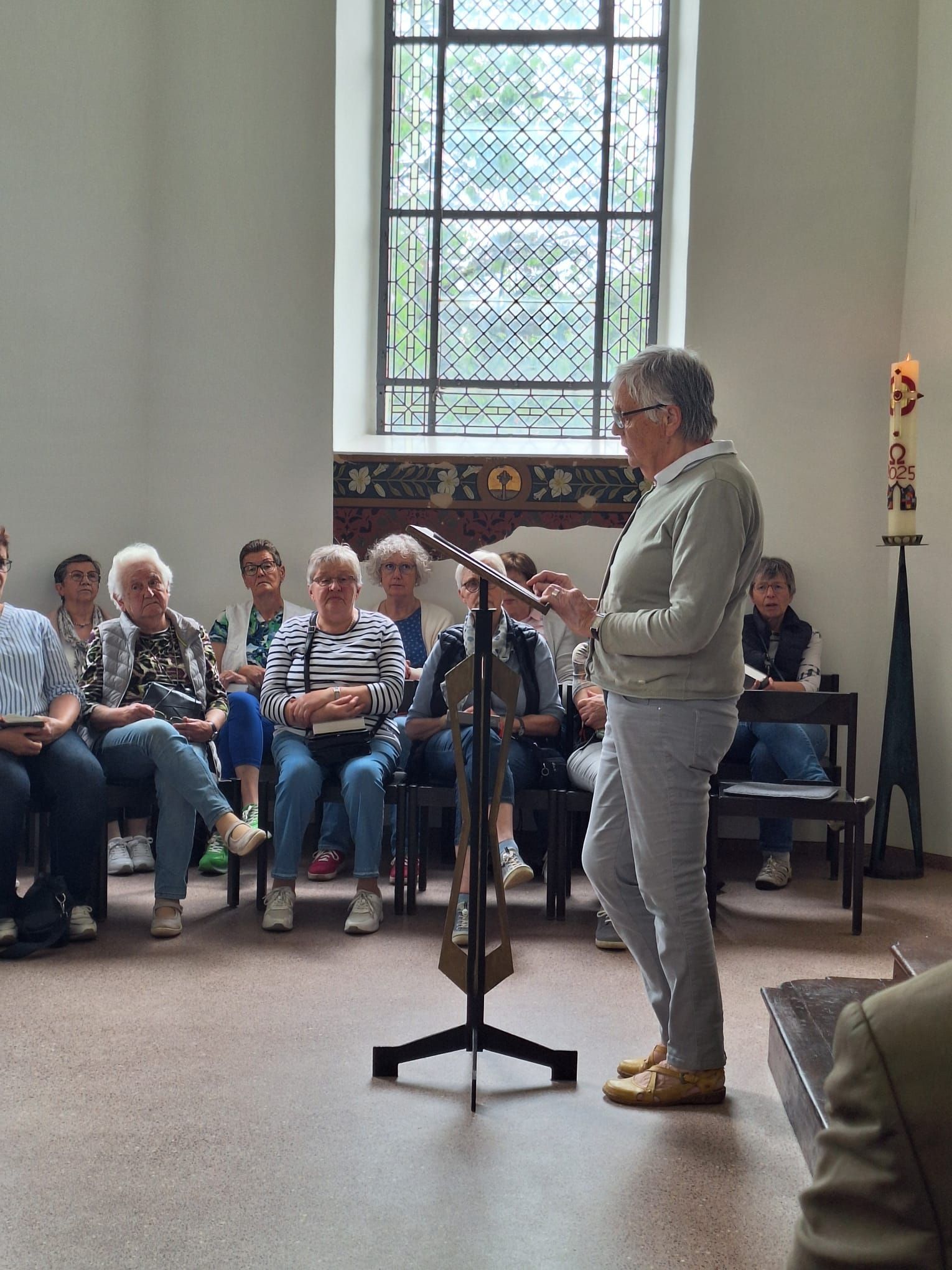 Eine Frau steht vor einem Mikrofon vor einer Gruppe von Menschen, die auf Stühlen sitzen.