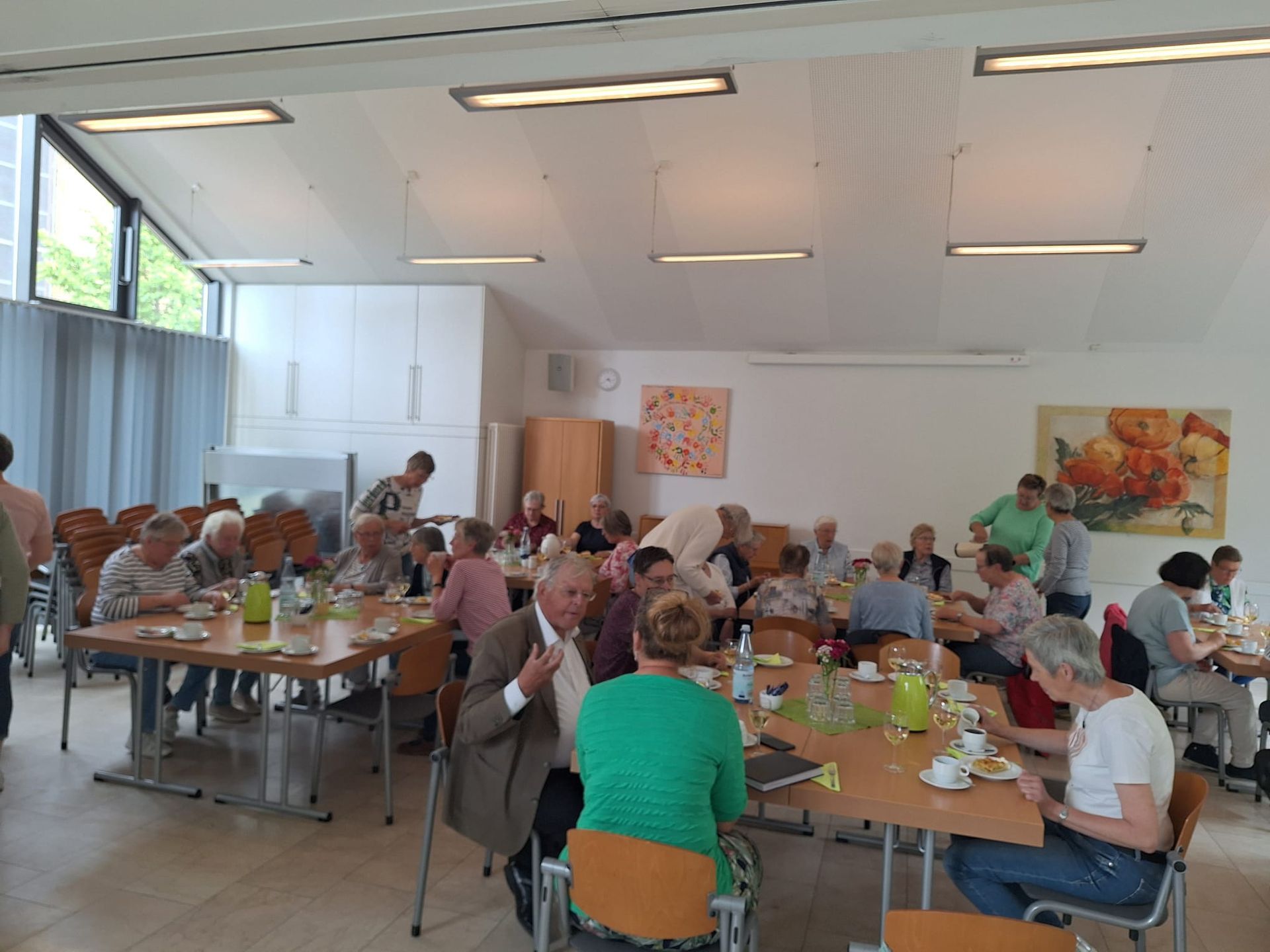 Eine Gruppe von Menschen sitzt in einem großen Raum an Tischen.