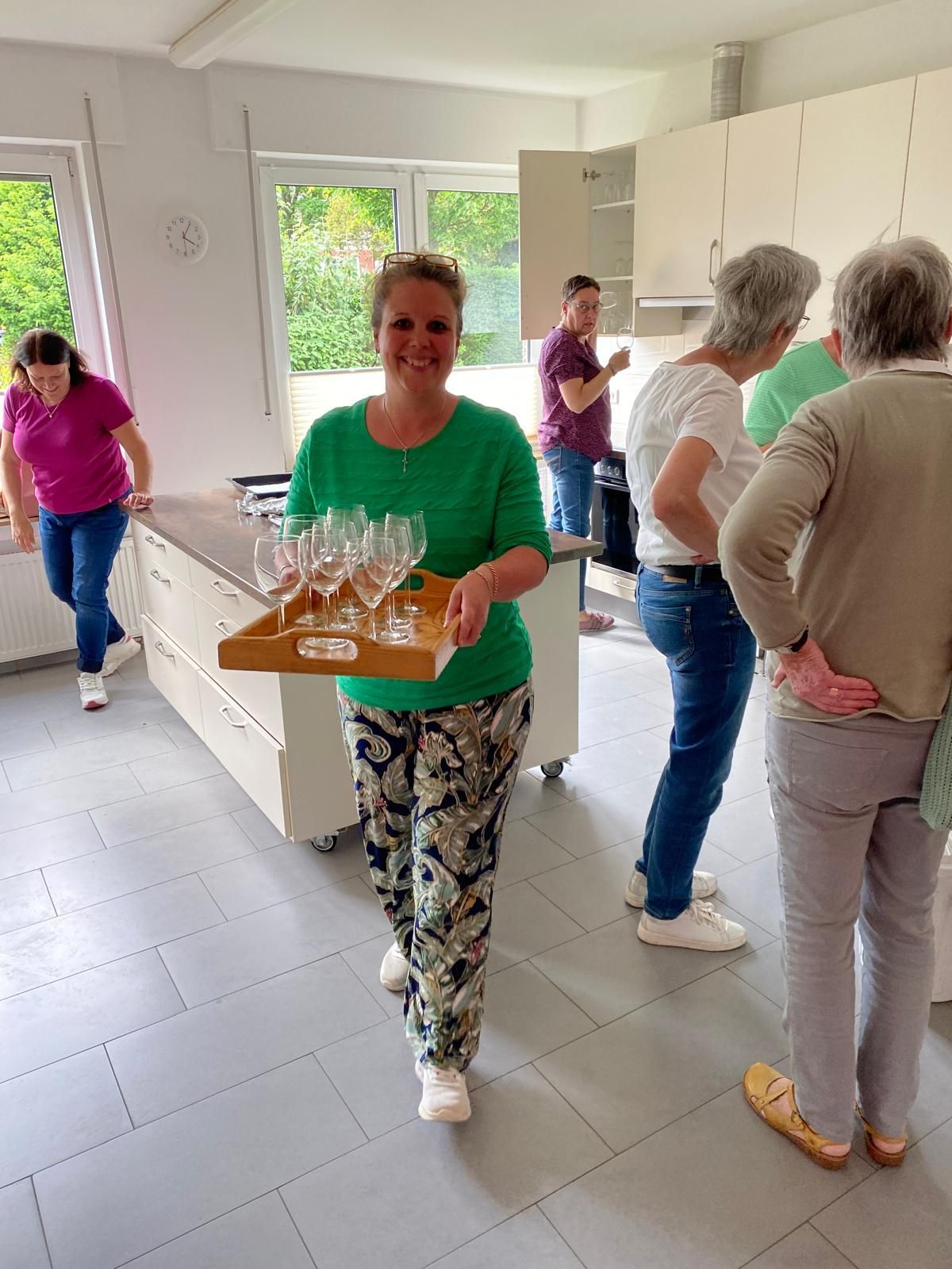 Eine Frau trägt ein Tablett mit Weingläsern in einer Küche.