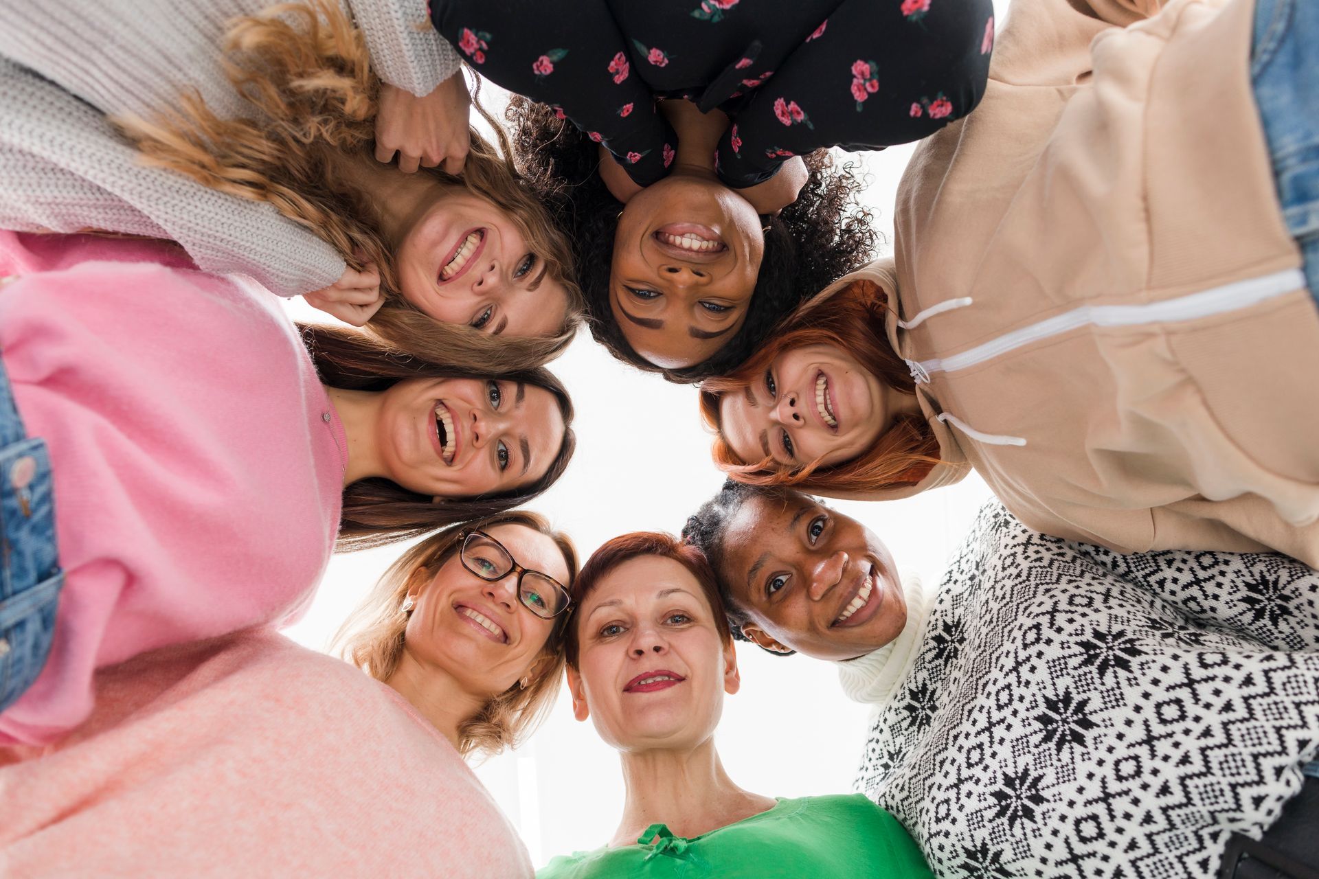 Eine Gruppe von Frauen steht im Kreis und schaut nach unten in die Kamera.
