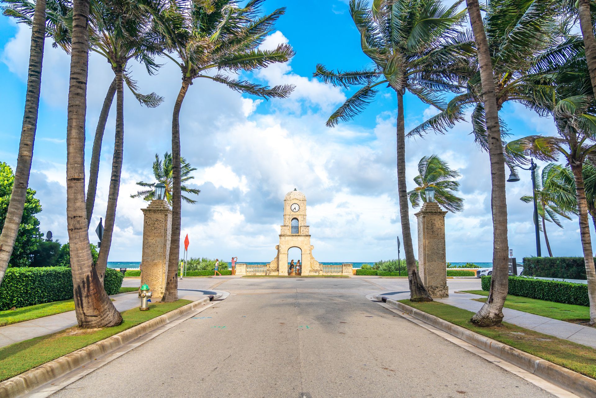 There is a statue in the middle of the road surrounded by palm trees.