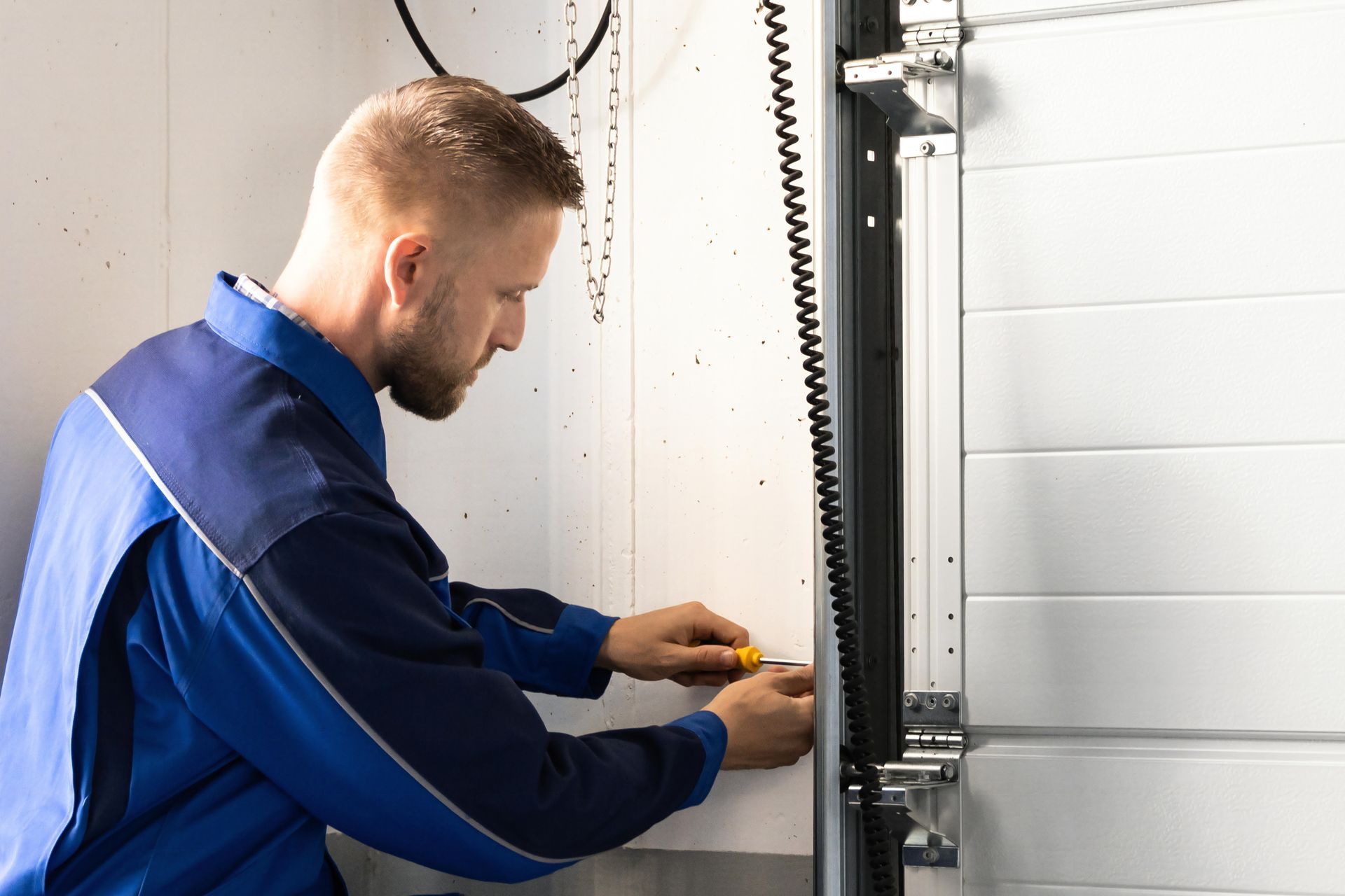 Worker tightening components on a garage door track as part of maintenance Worker tightening components on a garage door track as part of maintenance