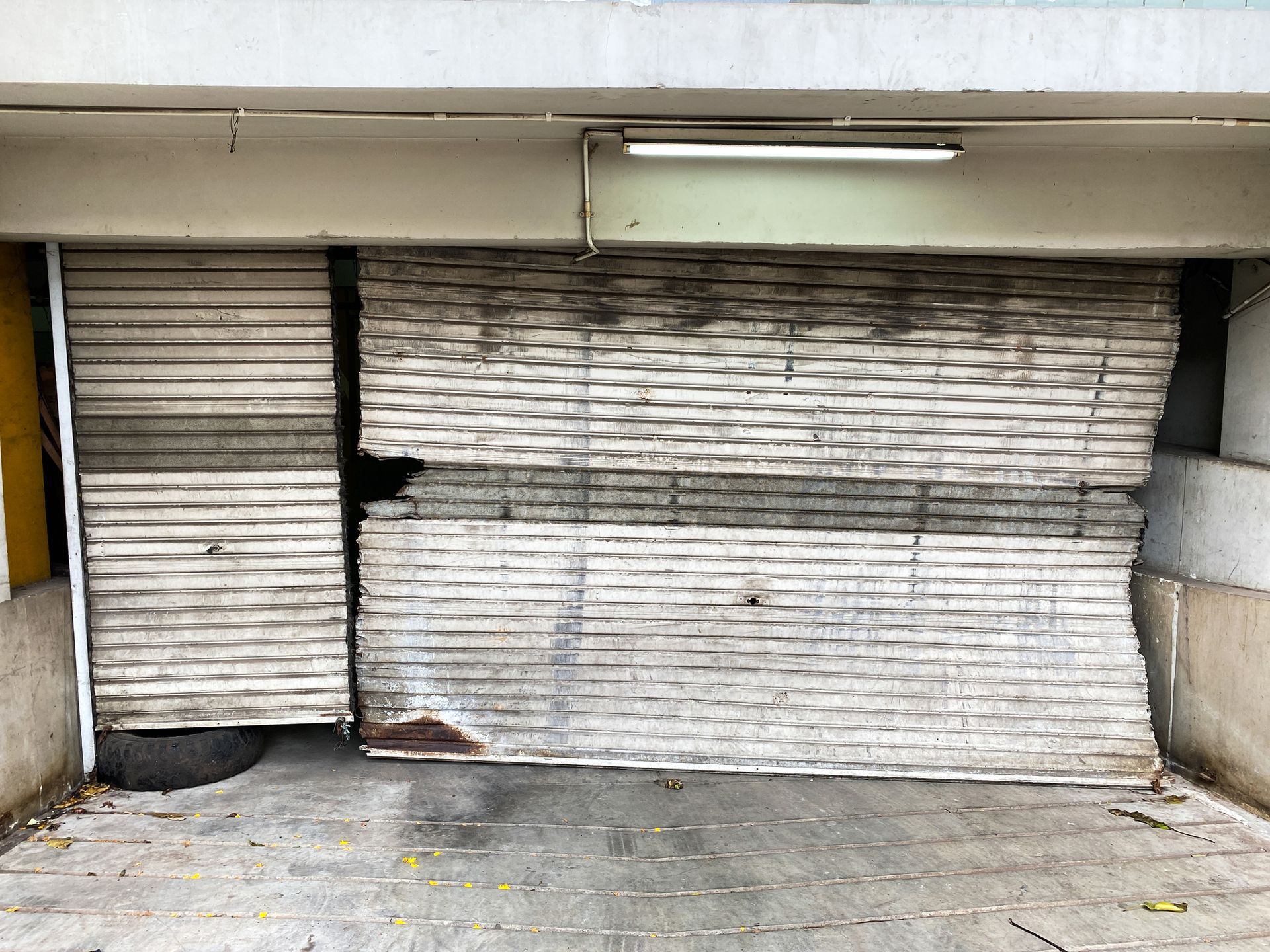 Damaged, white, metal roller shutter on a building's storefront. Partially collapsed, dark stains.