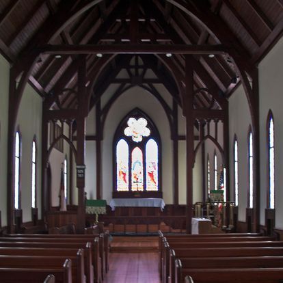 Interior of a church with stained-glass window, wooden pews, and dark wood beams.