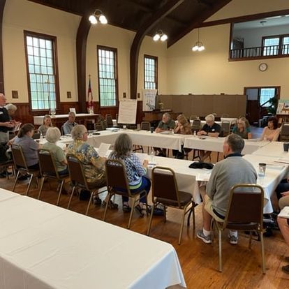 People seated at table in parish hall, likely a meeting or conference.