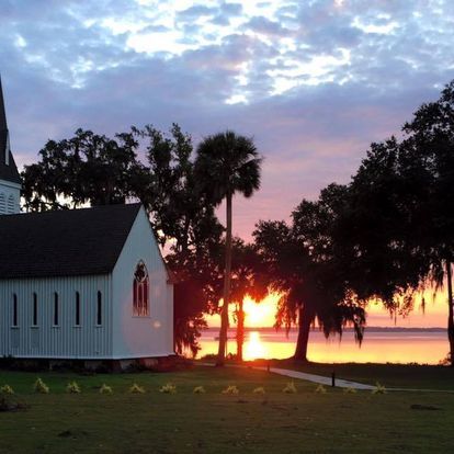 White church at sunset overlooking water with palm trees.