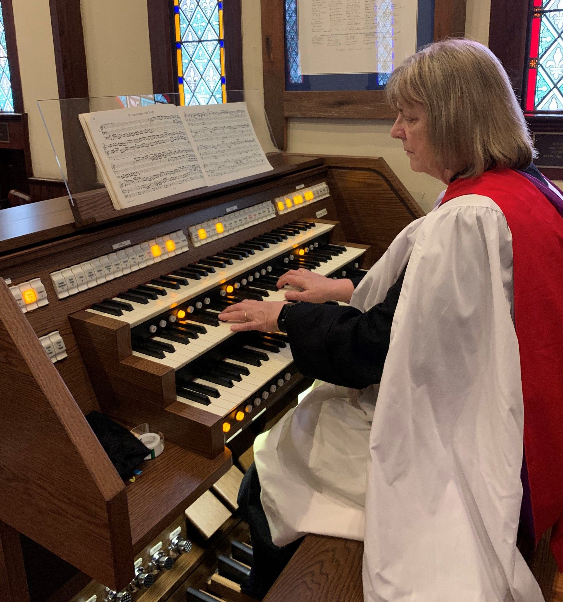 Woman playing an organ, wearing a red and white robe. Inside a church.