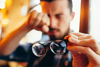 Man holding a pair of frames while rubbing eye