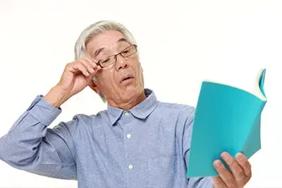 Man rubbing his eye while reading a book
