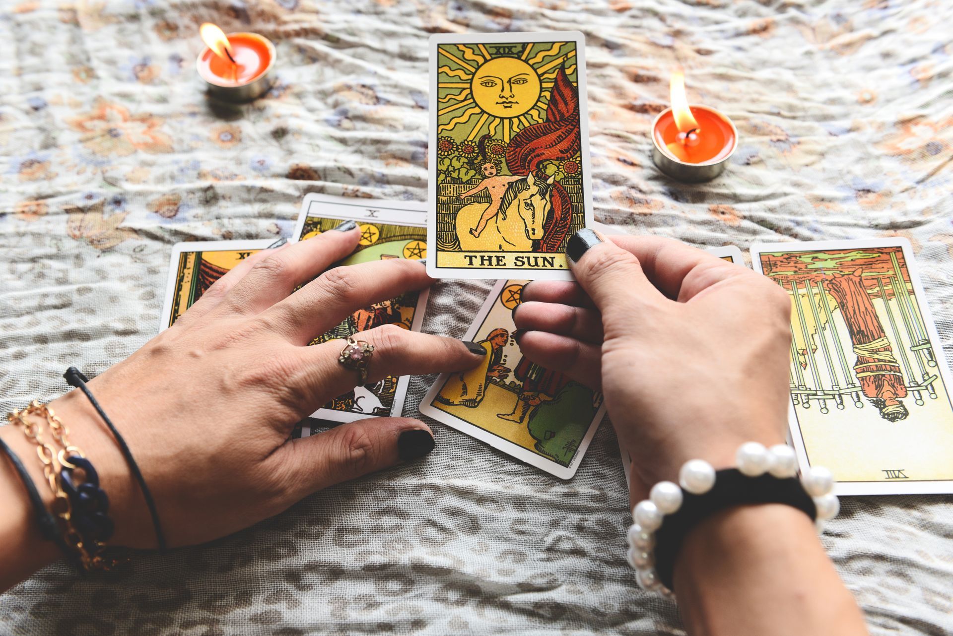 Hands holding a fan of colorful tarot cards on a white table near candles.