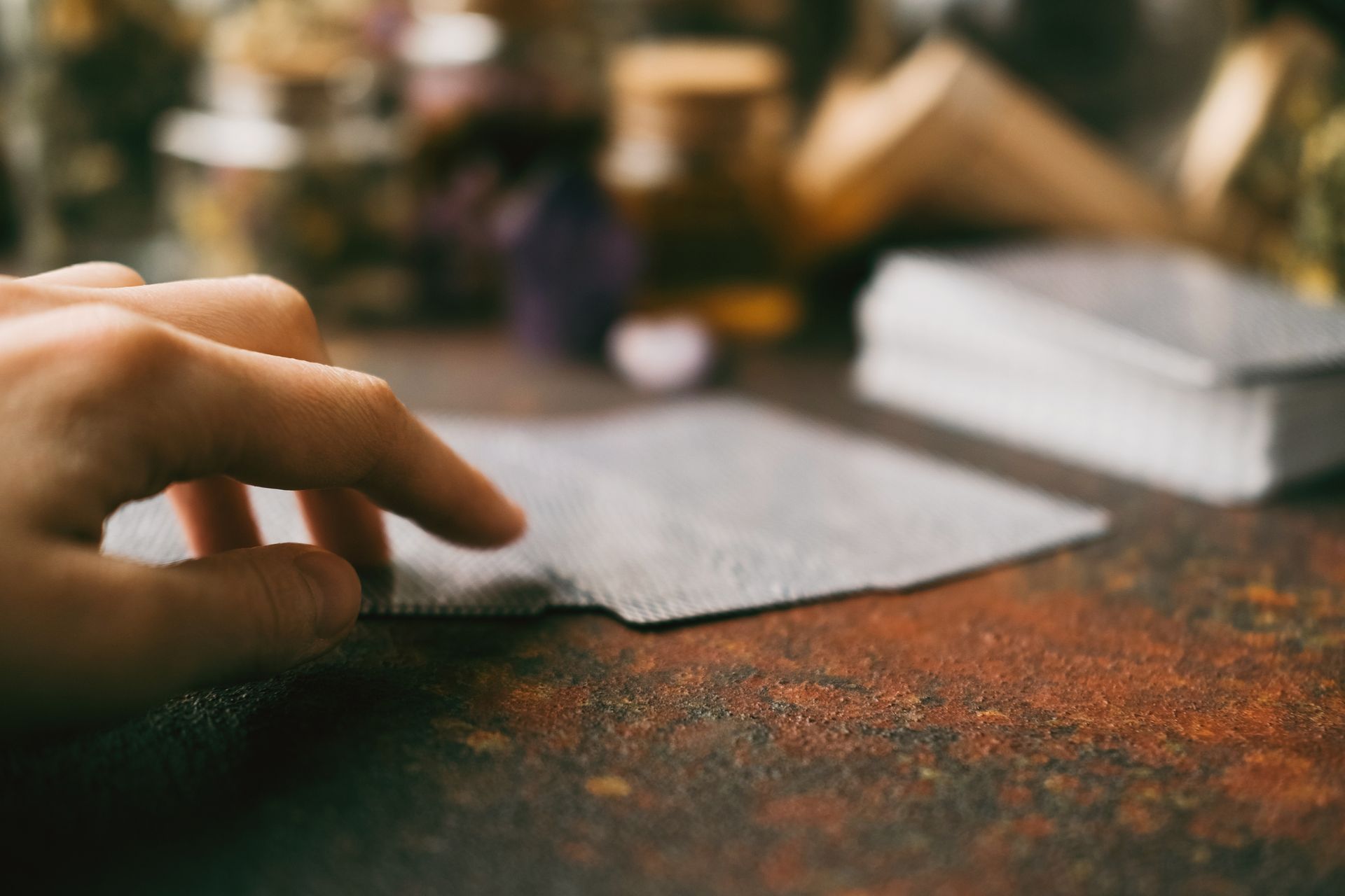 Female hand touching Tarot cards lying on rusty surface against blurred bottles. Female hand touching Tarot cards lying on rusty surface against blurred bottles.