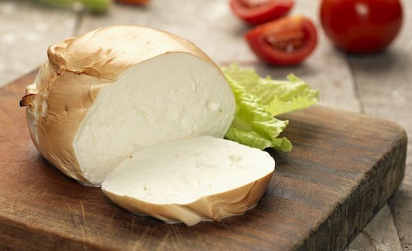 Formaggio Zizzona di Battipaglia bianco grande con pomodorini e basilico su un tagliere di legno.