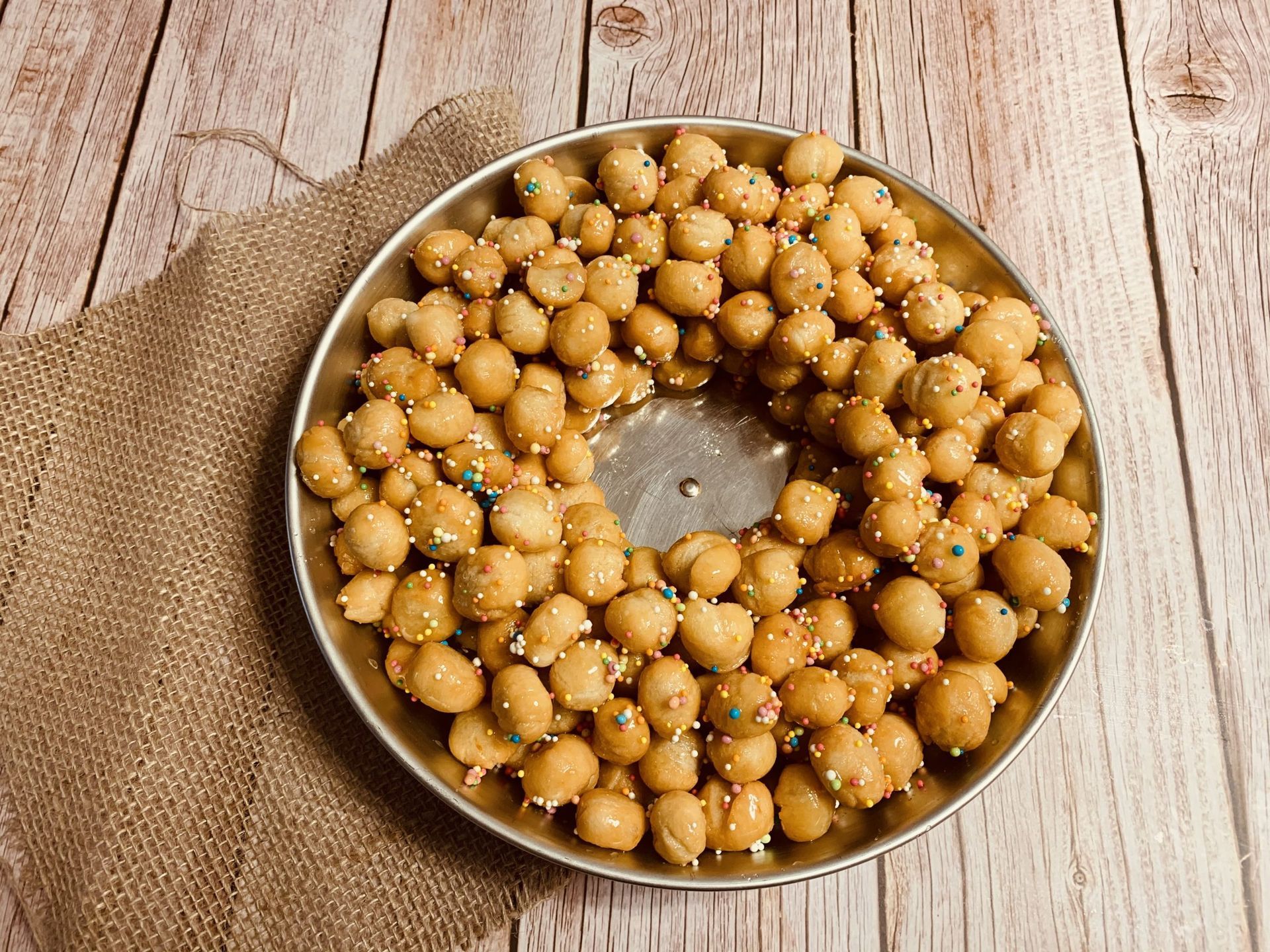 Un piatto di pasticcini dorati e sferici, ricoperti di granella colorata, su una superficie di legno.
