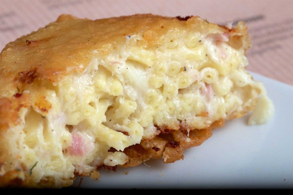 Pallina di risotto fritta tagliata a metà, che rivela il ripieno cremoso e i piselli, su carta marrone. Sullo sfondo, una ciotola di piselli.