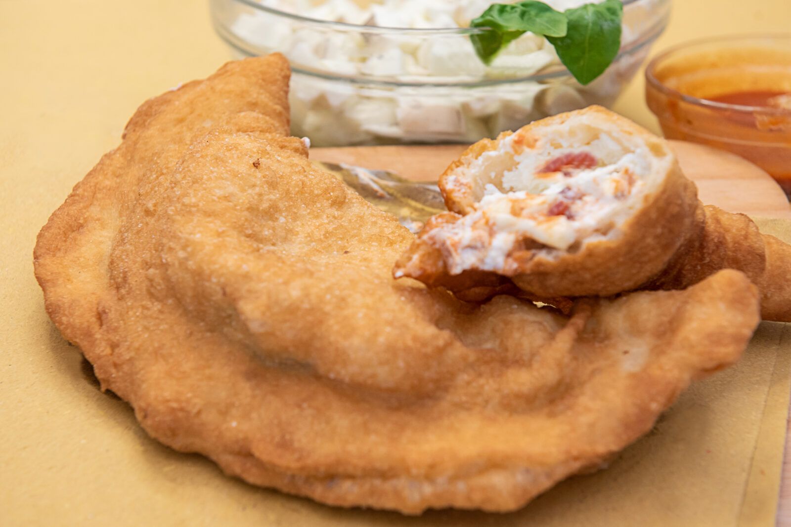 Tasca di pane fritto, ripiena di salame e formaggio su un piatto, con pomodoro e vino rosso sullo sfondo.