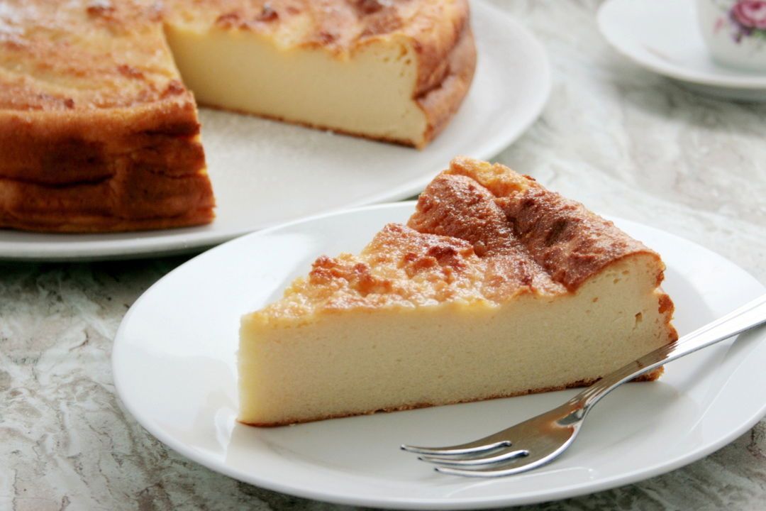 Cheesecake con una fetta tagliata, spolverata di zucchero a velo, su un piatto con succo d'arancia.