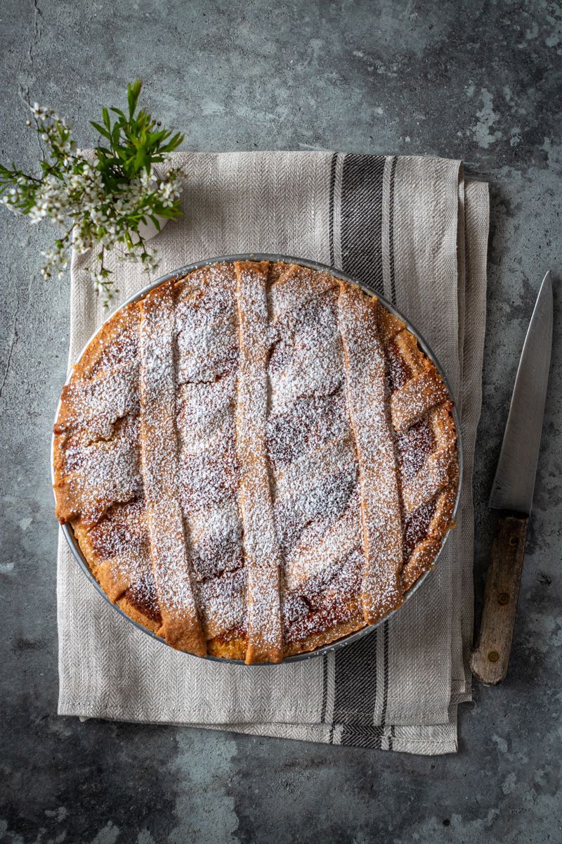 Un uomo in camice nero da chef sorride, tenendo in mano una grande palla bianca, vicino a una scatola. Bar con bottiglie.