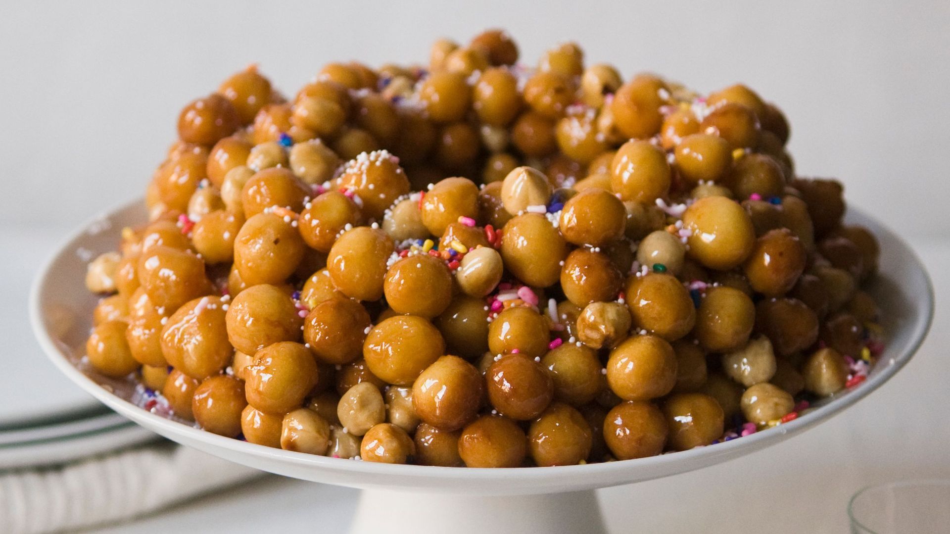 Un uomo con occhiali, guanti neri e grembiule morde un oggetto bianco ricoperto di rosso all'aperto.