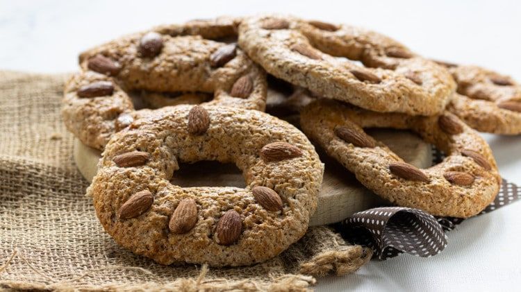 Un uomo con occhiali, guanti neri e grembiule morde un oggetto bianco ricoperto di rosso all'aperto.