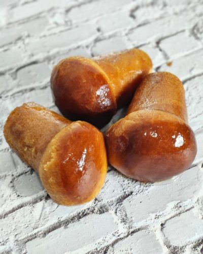 Un uomo con occhiali, guanti neri e grembiule morde un oggetto bianco ricoperto di rosso all'aperto.