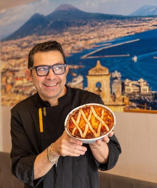 Una crostata di ricotta rotonda, con una decorazione a grata, su una superficie di legno, con bastoncini di cannella e un'arancia.