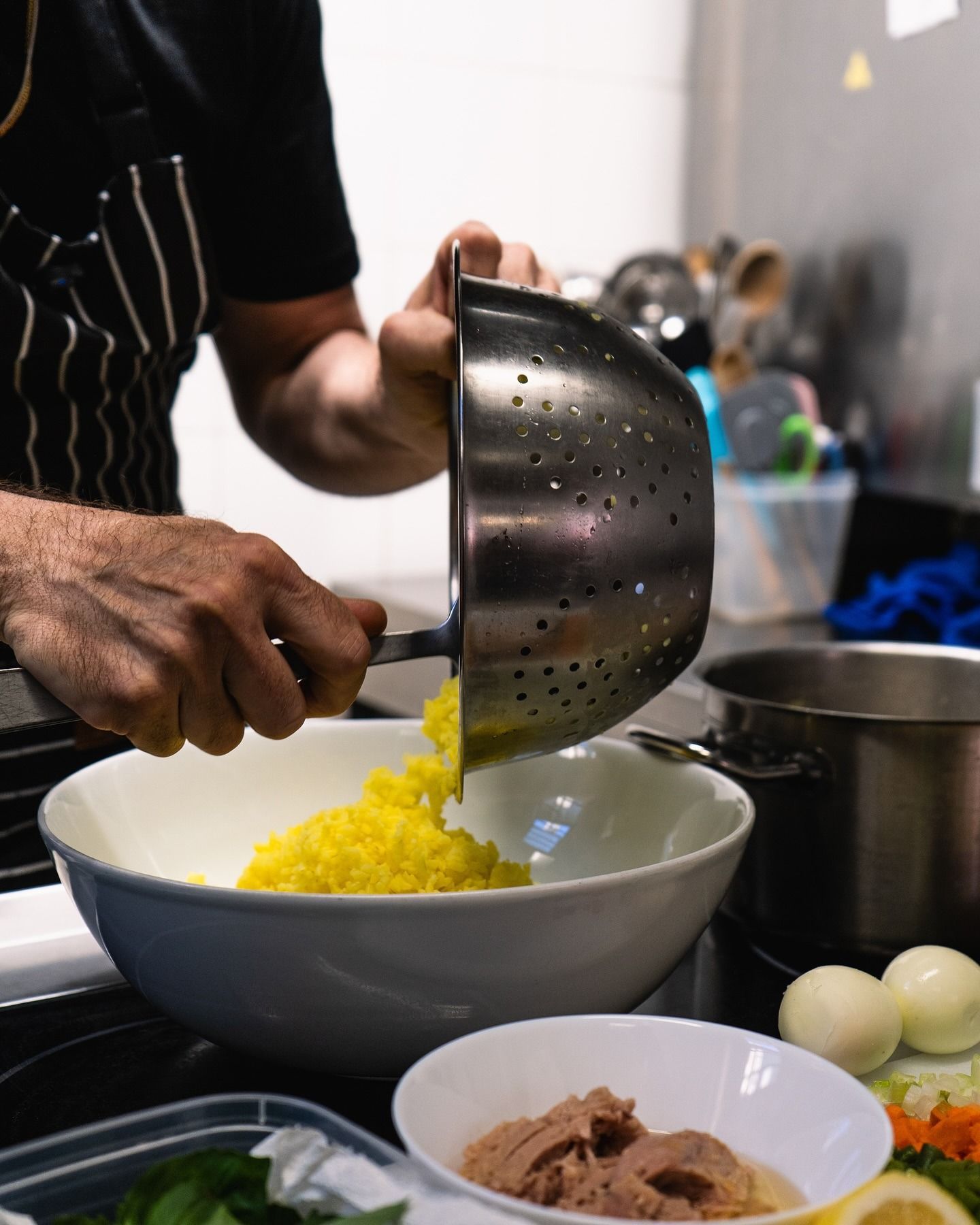 Un uomo in camice nero da chef sorride, tenendo in mano una grande palla bianca, vicino a una scatola. Bar con bottiglie.