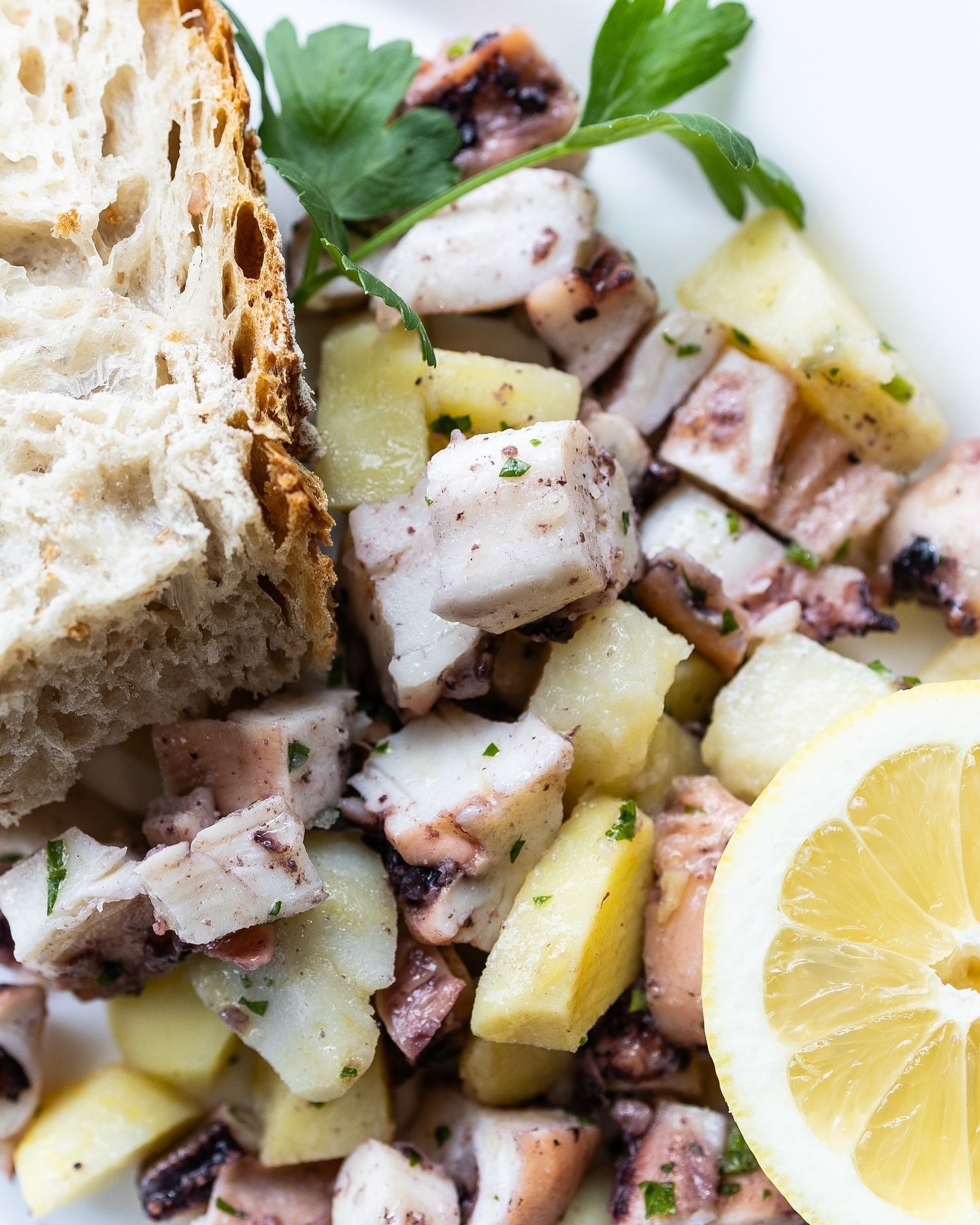 Un uomo con occhiali, guanti neri e grembiule morde un oggetto bianco ricoperto di rosso all'aperto.
