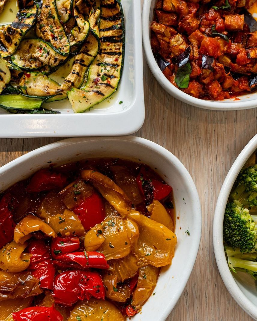 Piatti di verdure assortite in ciotole bianche: zucchine grigliate, melanzane, peperoni e broccoli.