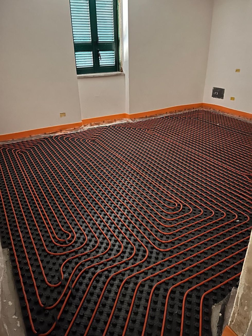 Tubi per riscaldamento a pavimento radiante installati a griglia su pannelli isolanti neri in una stanza non rifinita.