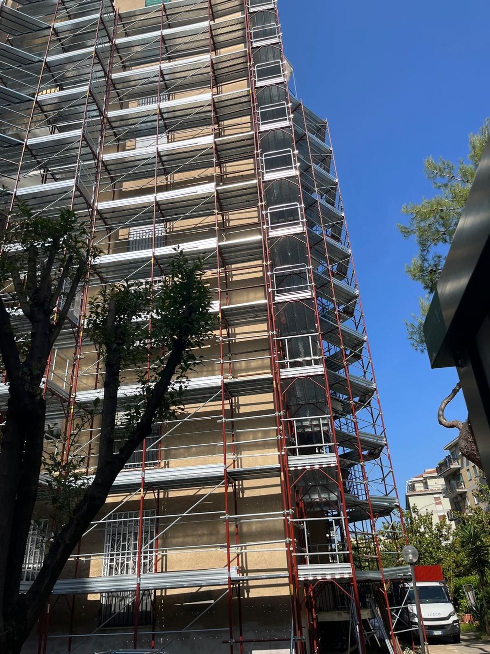 Un alto edificio residenziale ricoperto da un'estesa impalcatura metallica sotto un cielo azzurro e limpido.