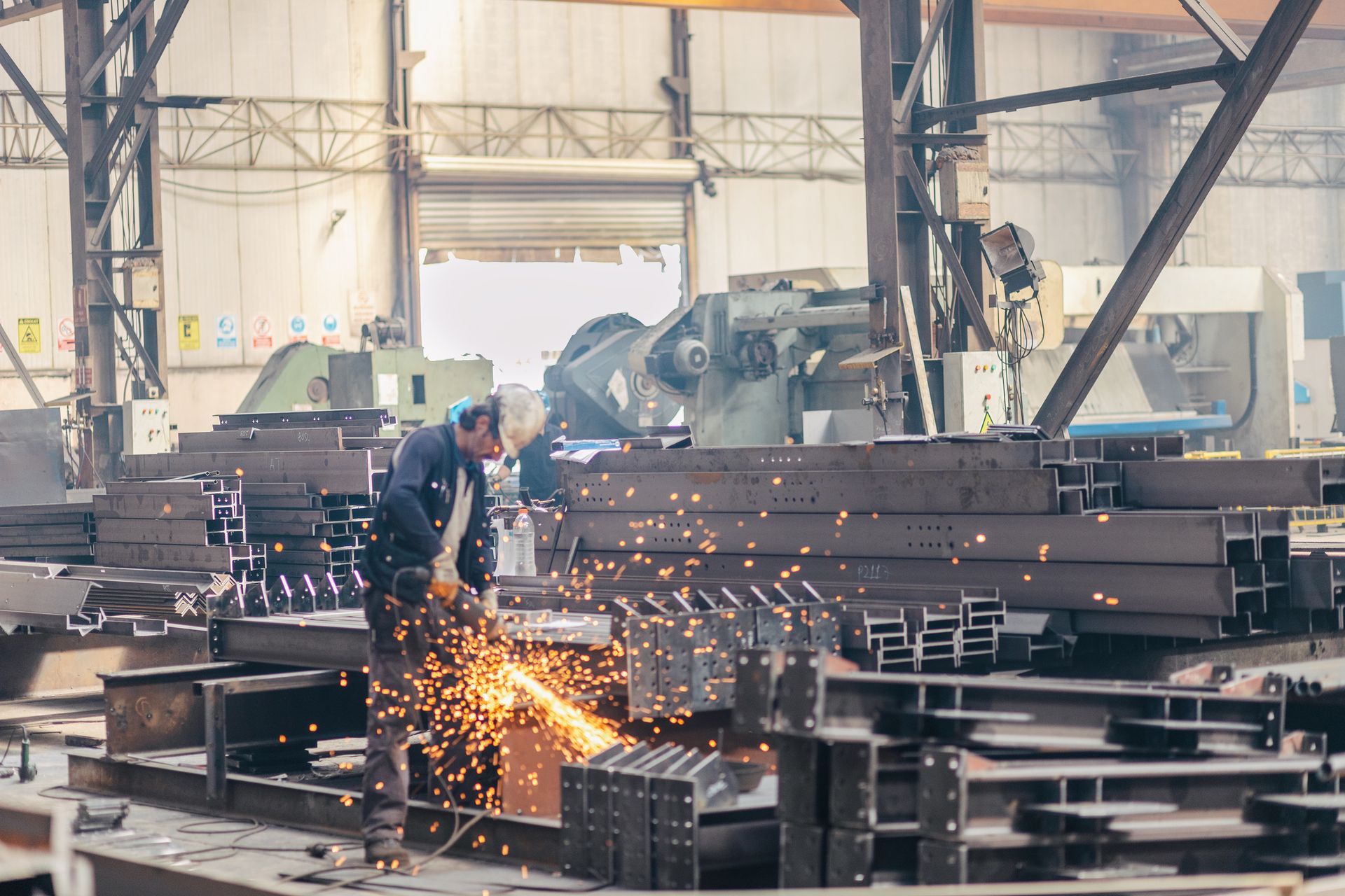 : A steel fabricator in a factory creates sparks while working on a piece of steel stock. : A steel fabricator in a factory creates sparks while working on a piece of steel stock.