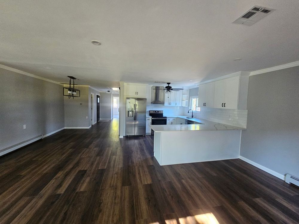 A large empty room with hardwood floors and a kitchen in the background.