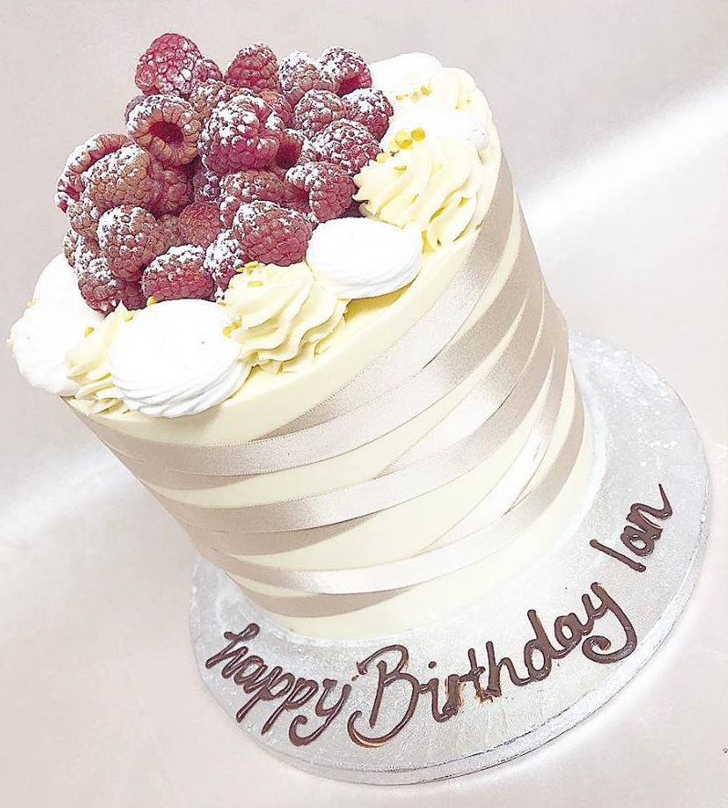 A happy birthday cake with raspberries on top
