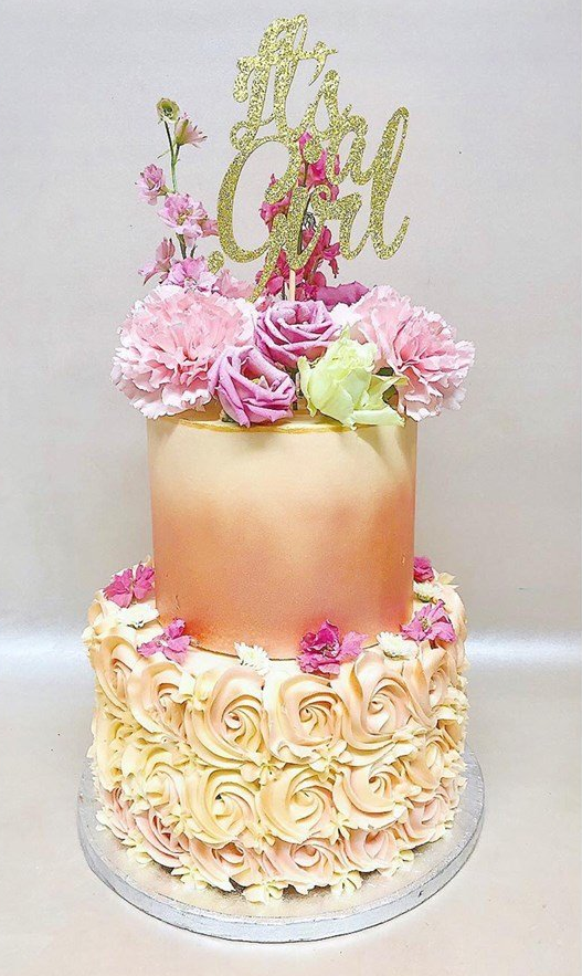 A cake with flowers on top of it and a topper that says `` it 's a girl ''.