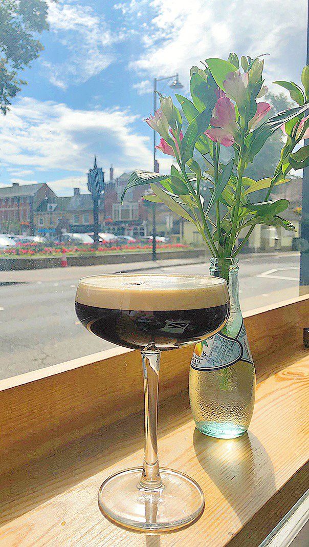 A cocktail is sitting on a wooden table next to a vase of flowers.