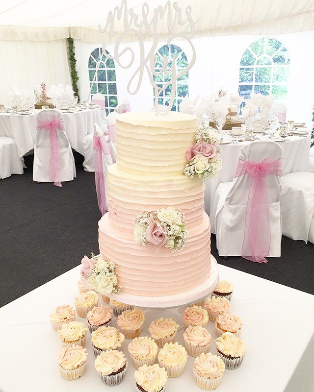A wedding cake and cupcakes are on a table in a tent.