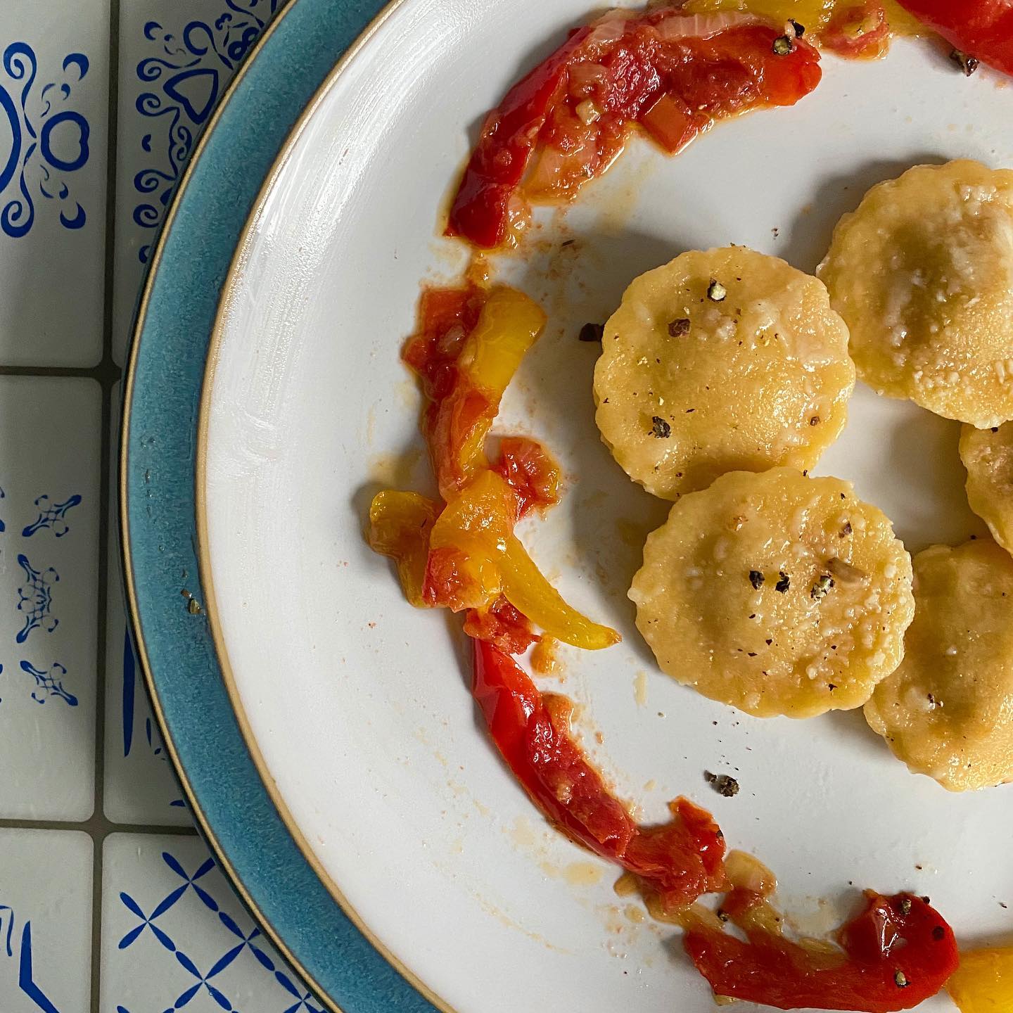A white plate topped with ravioli and red peppers