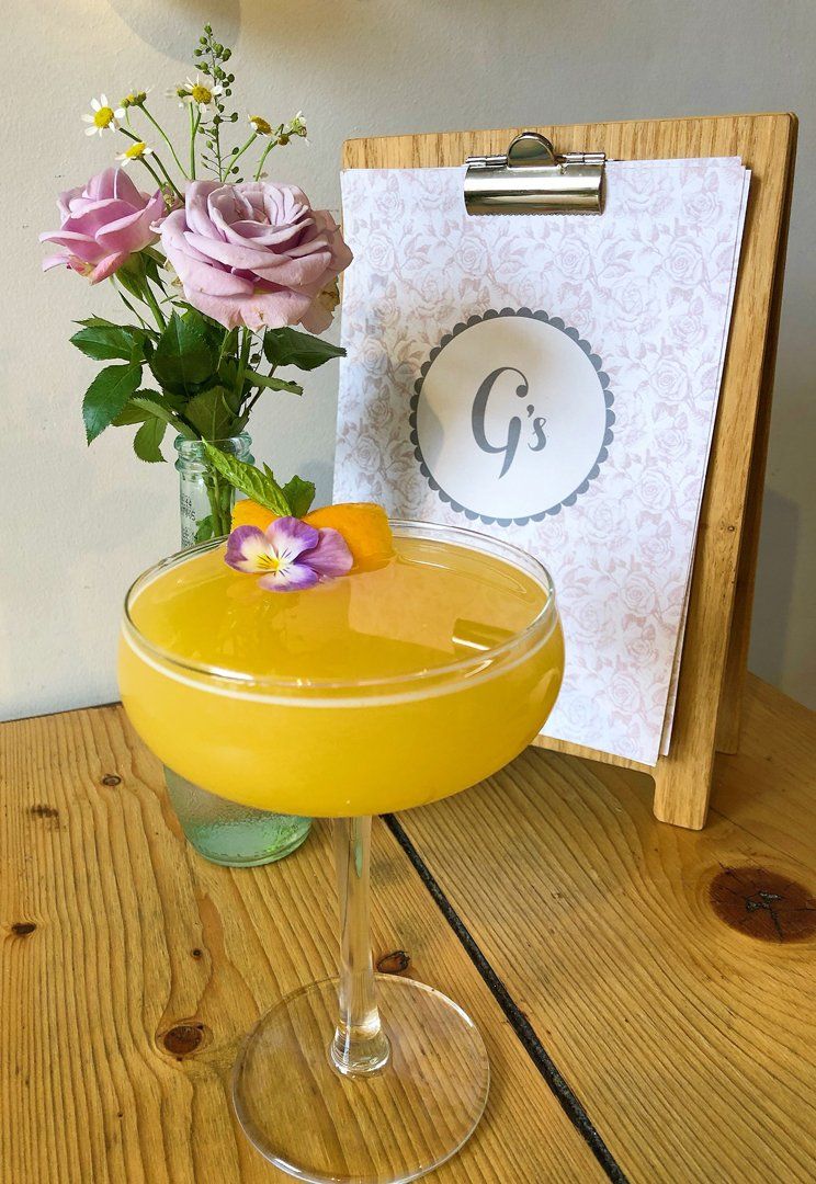 A cocktail next to a vase of flowers on a wooden table.