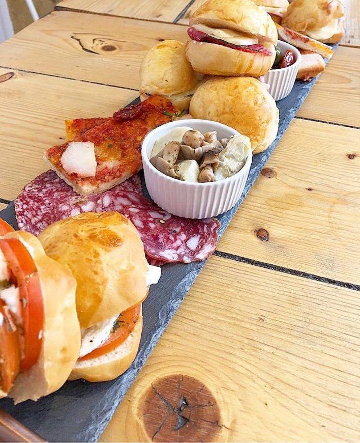 A wooden table topped with a tray of food including sandwiches and a bowl of mushrooms.