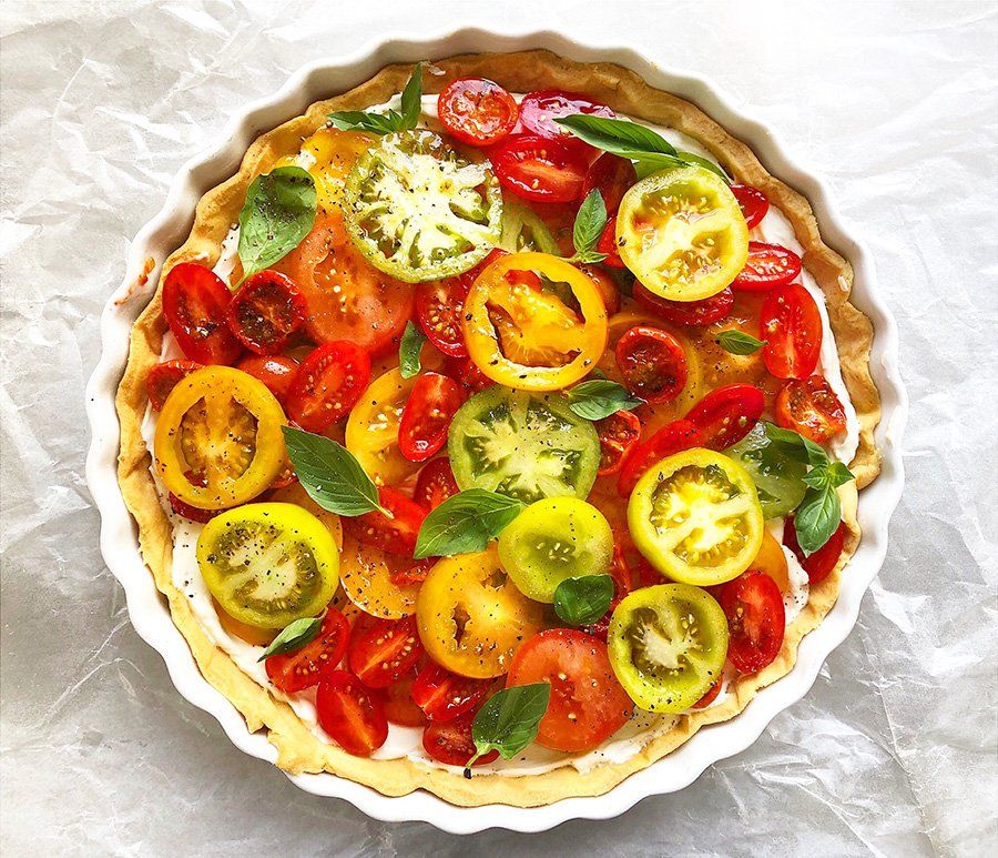 A pie filled with tomatoes and basil is sitting on a table.