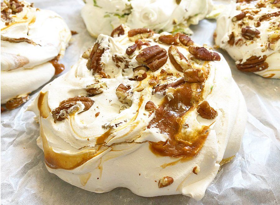 A close up of a meringue covered in caramel and pecans on a table.