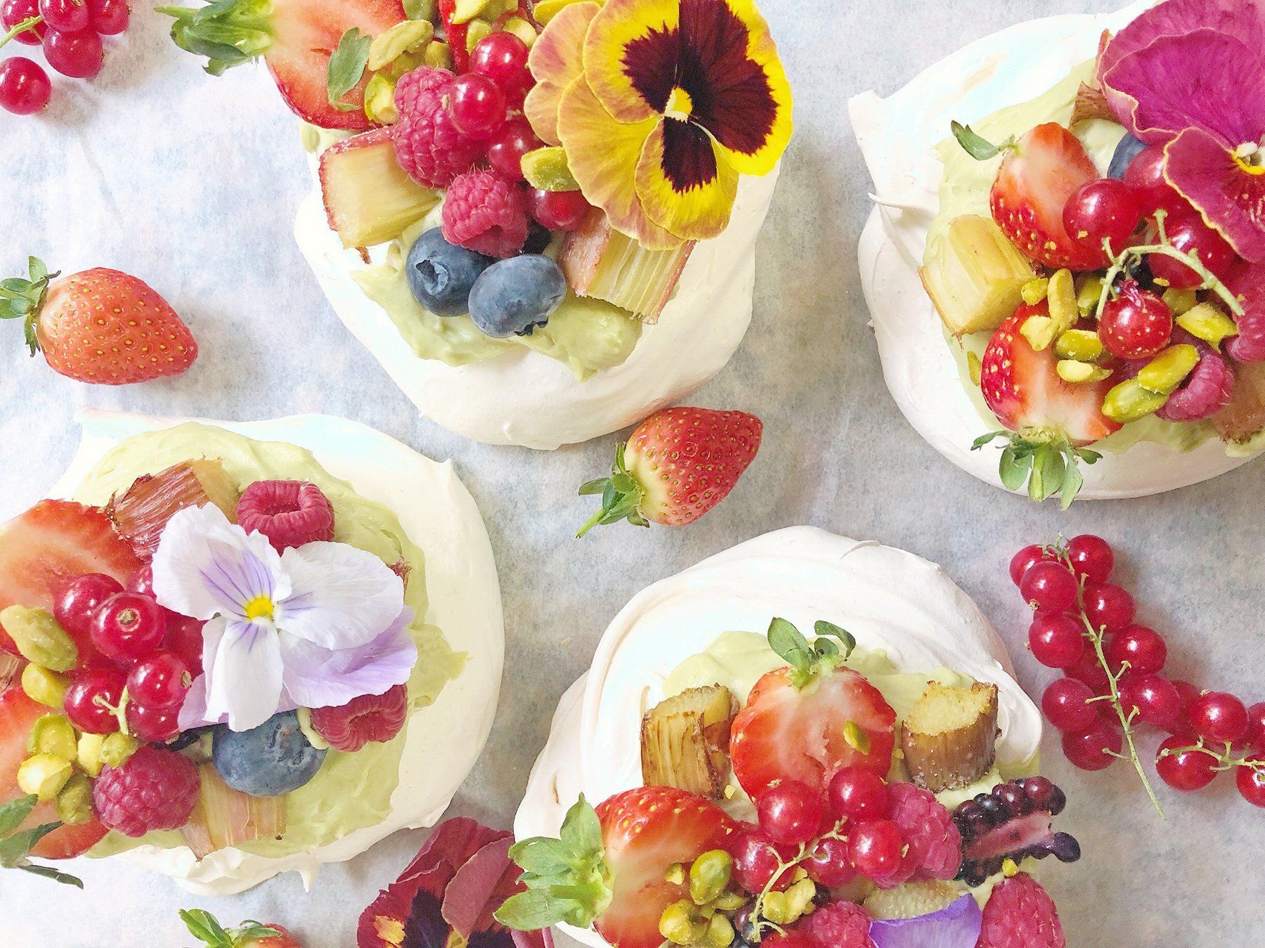 Four meringue cups filled with fruit and flowers on a table.